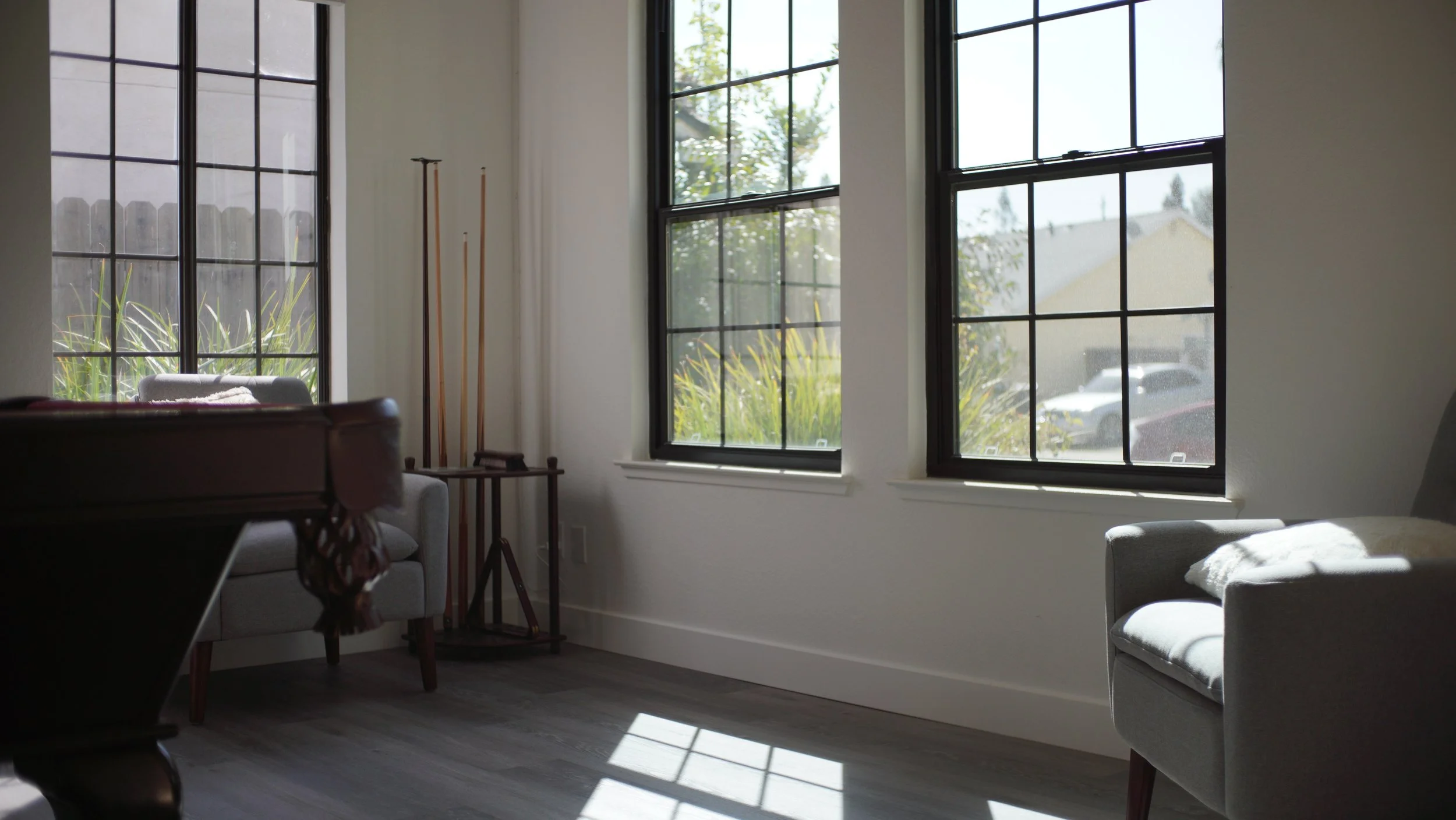 A common room at Beacon Support Homes with a pool table, cue rack, and armchairs beside two tall windows with daylight across the floor