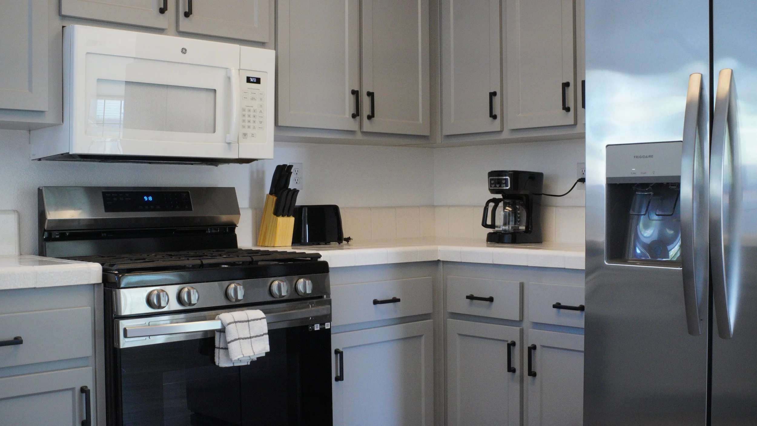 The shared kitchen at Beacon Support Homes: light gray cabinets, a gas range, coffee maker on the counter, and a stainless steel refrigerator